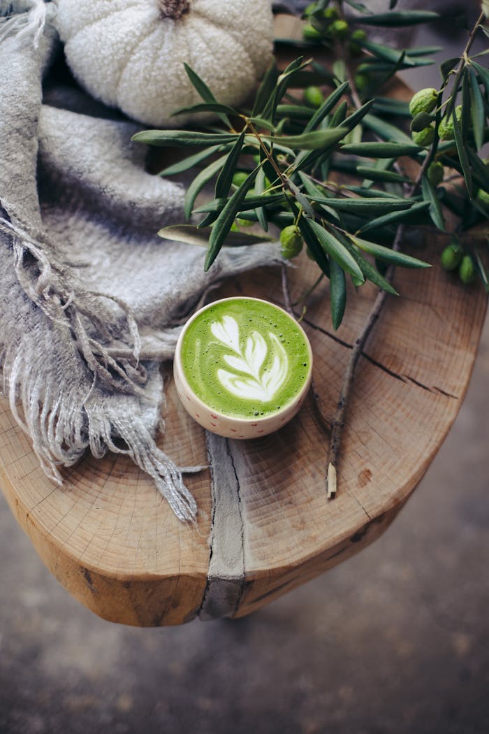 A warm matcha latte with latte art on a rustic table adorned with autumn decor.